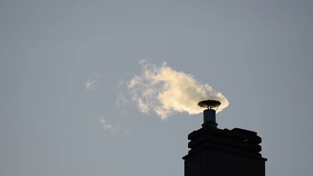 Footage of a chimney of the condominium heating system. The low rays of the winter sun enhance the puffs of smoke that increase and decrease depending on the engagement of the boiler.