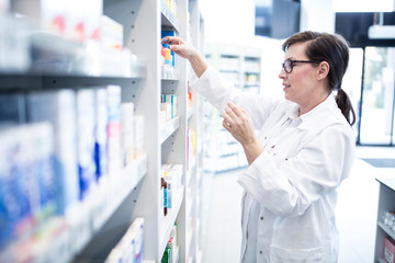 Pharmacist sorting medicine at shelf in pharmacy