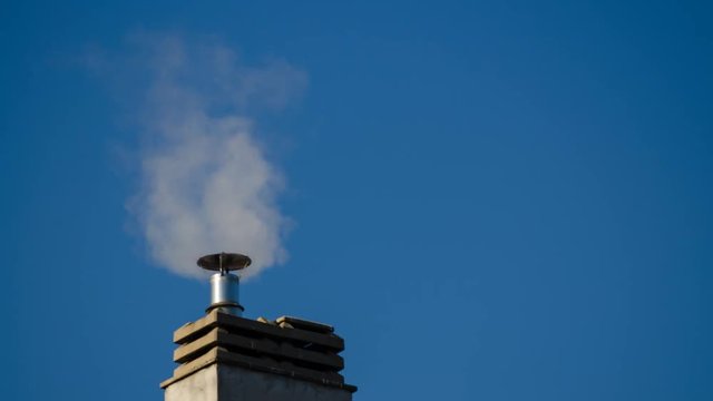 Timelapse 4k of a chimney of the condominium heating system. The low rays of the winter sun enhance the puffs of smoke that increase and decrease depending on the engagement of the boiler. 