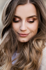 Portrait of beautiful girl after beauty salon with shiny make up, bronze sunburn, long eyelashes, plump lips and long wavy hair, sensuality looking down. Concept ob beauty and glamour.