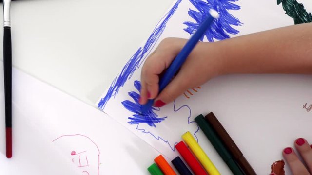 The girl sits at the white table and draws a picture with colored felt-tip pens. Homemade creativity