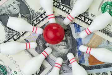 Red winning bowling strike ball surround with knocked down pins on pile of US dollar banknotes money, financial success target concept, goals on investment or profit in stock market concept