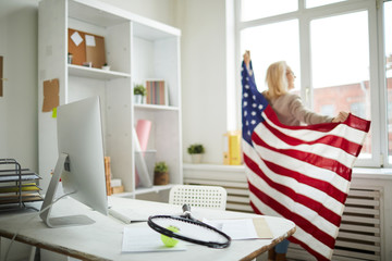 Back view portrait of contemporary adult woman holding American flag at workplace, copy space