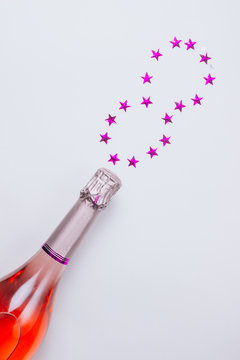 Champagne bottle with confetti stars on white background.