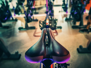 Closeup modern Bike Saddle with blurred row of training exercise bikes and warm light. Fitness cycling indoor concept.