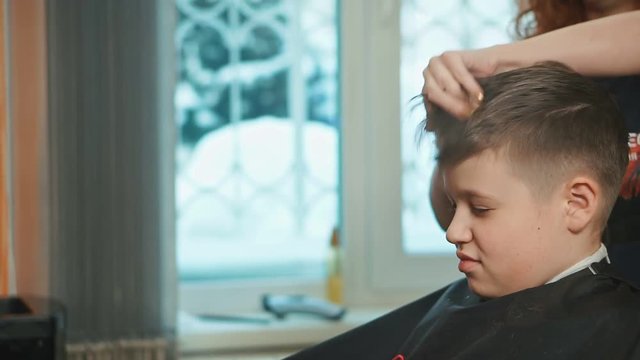 Hairdresser makes a trendy haircut and wets the hair on the boy's head