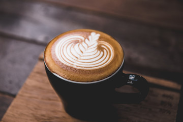 Cup of cappuccino with latte art in black cup with wooden background