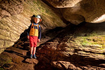 Boy inside the ancient cave with stone walls with additional lighting. Texture of a stone wall in a cave.
