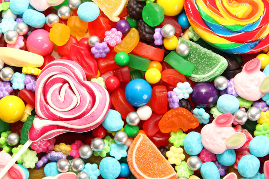 Assorted variety of sweet sugar candies includes lollipops, gummy bears, gum balls and sugar fruit slices. Flat lay, top view. 