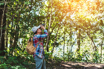 Young man with backpack and holding a binoculars looking in forest