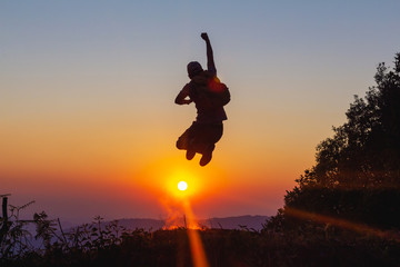Silhouette of happy hiker man jumping on mountain at sunset time