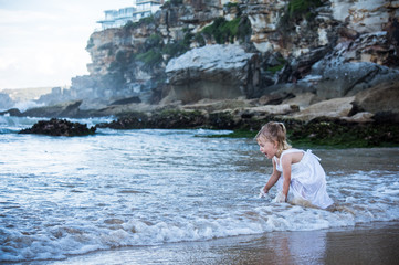 little girl playing with water in a beautiful beach with rocks in Australia