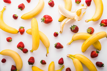 Fresh strawberries and bananas scattered on white background, top view