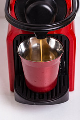 Red coffee machine pouring coffee on a red metal coffee cup