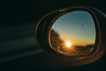 Yellow bright sun shining on an oval black car mirror reflection