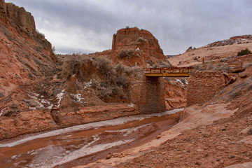 Freezing creek with prefabricated one lane narrow metal bridge with guardrails for vehicle crossing between red rocks in American Southwest