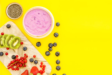 Obraz na płótnie Canvas Preparing healthy fruit smoothie. Acai smoothie bowl near cutting board with fresh fruits, berries, chia seeds on yellow background top view space for text