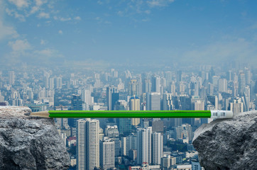 Green pencil on rock mountain over modern city tower, office building and skyscraper, Business success strategy plan concept