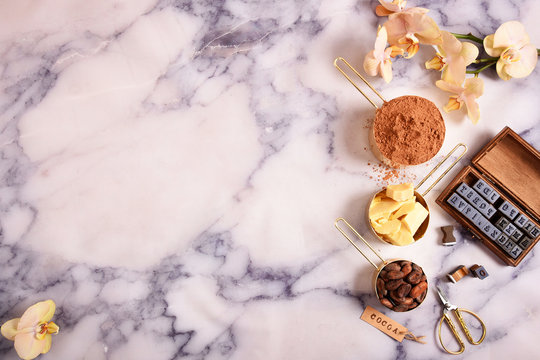 Cocoa, cocoa butter and cocoa beans, chocolate in gold containers on a marble surface. Flat lay. Place for text.