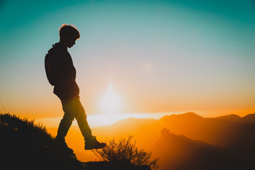 Silhouettes of little boy hiking in sunset mountains