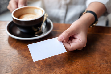 A woman holding and giving a blank empty business card to someone while drinking coffee