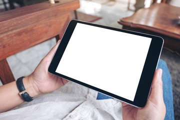 Mockup image of a woman's hands holding black tablet pc with blank white screen horizontally while sitting in cafe