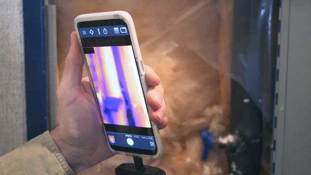Infrared thermal camera attached to a smartphone checking the insulation and pipes of a home to find leaks.
