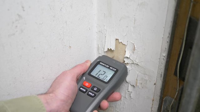 Water damaged wall being checked with a moisture reader.