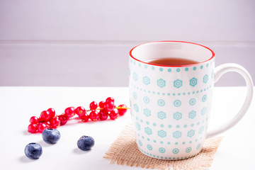cup of black tea with berries on a white wooden background