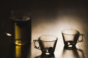 Hot herbal brewed tea in transparent teapot and two cupson wooden background.