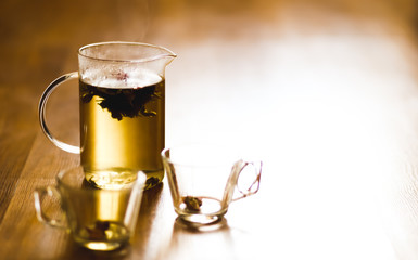 Hot herbal brewed tea in transparent teapot and two cupson wooden background.