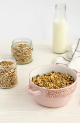 Homemade muesli in a bowl and glass jar, a bottle of milk on a white background