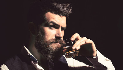 Man with beard holds glass brandy. Bearded drink cognac. Sommelier tastes drink. Man holding a...