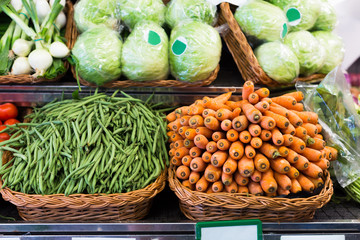Green beans and carrots in wicker baskets on counter of vegetable store