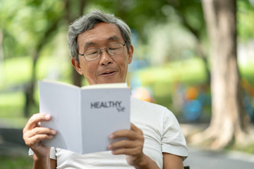 Asian senior man reading Healthy Life book alone in the park