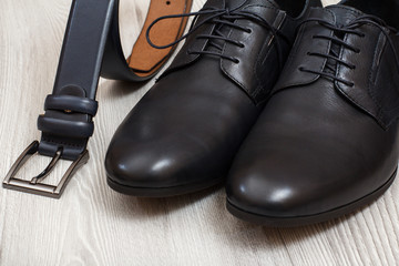 Pair of black leather men's shoes and leather belt for men on wooden background.