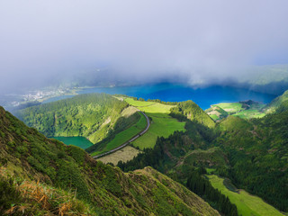 Obraz premium Stunning view on volcanic lakes. Green Lagoa de Santiago and blue Lagoa Azul with Sete Cidades village, partially covered by fog mist and clouds. Sao Miguel in the Azores, Portugal