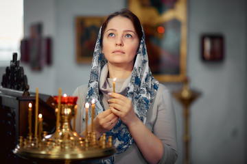 lifestyle woman lights candles in the Church, praying in front of the icon