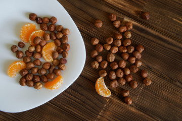 Peeled hazelnuts and slices of mandarin in a white plate on a natural wooden surface of pine boards