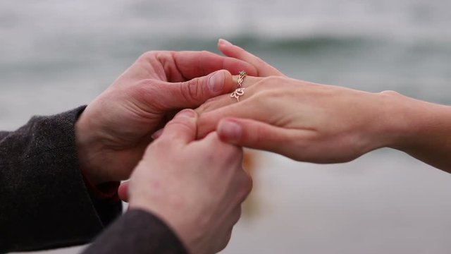 Close-up senior female hand getting engagment ring on her finger from elderly boyfriend. Senior male making marriage proposal to fiancee outdoors. Female looking and admiring her diamond ring slow mo