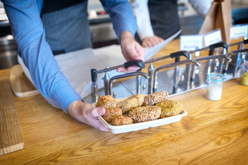 Takeaway lunch concept with waiter adding sauce on meatballs in fast food restaurant for customer, man hand holding casserole filled with baked meatballs.