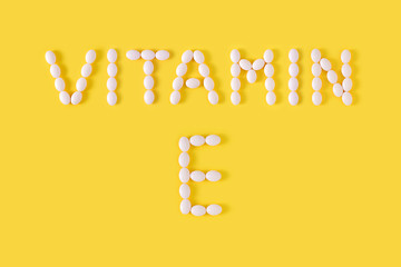 Vitamin E pills dropped from bottle on yellow background. Flat lay, top view, free copy space.