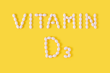 Vitamin D3 pills dropped from bottle on yellow background. Flat lay, top view, free copy space.