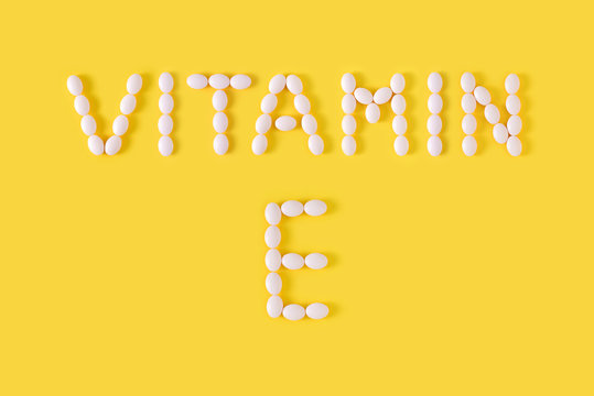 Vitamin E pills dropped from bottle on yellow background. Flat lay, top view, free copy space.