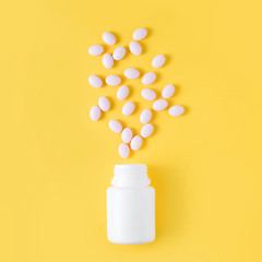 Pills dropped from bottle on yellow background. Flat lay, top view.