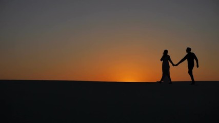 Man and woman pose embracing in morning sand desert closeup of heads and legs. Couple in love stand together in aura of sun holding each other.