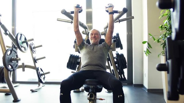 A senior man doing strength workout exercise in gym.