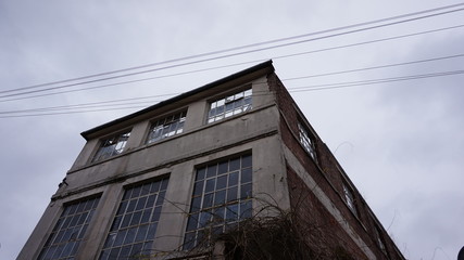 A crumbling abandoned building in Nottingham with no roof by the side of the road with large windows, gated off to be demolished, looking up towards a grey overcast sky