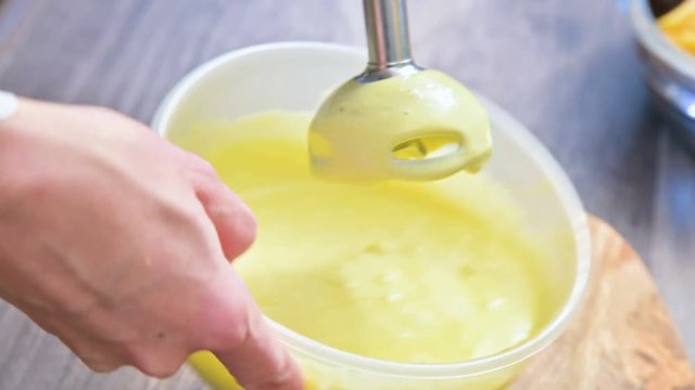 close-up whipping homemade mayonnaise with a blender in a plastic bowl