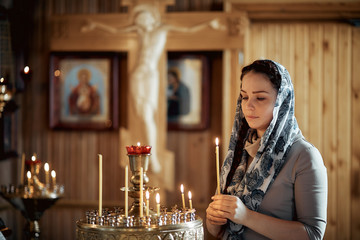 Russian beautiful Caucasian woman with red hair and a scarf on her head is in the Orthodox Church,...